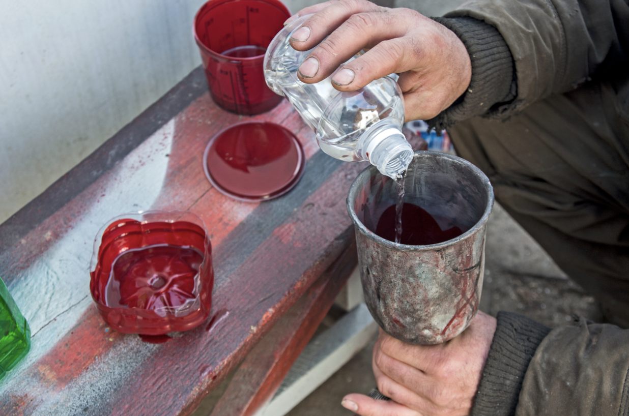 Close up of man's dirty hands adding clear liquid to can of paint as open cans of red paint sit in background